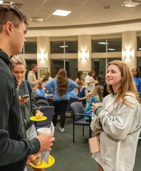 Two students talking indoors at Campus Ministry event.